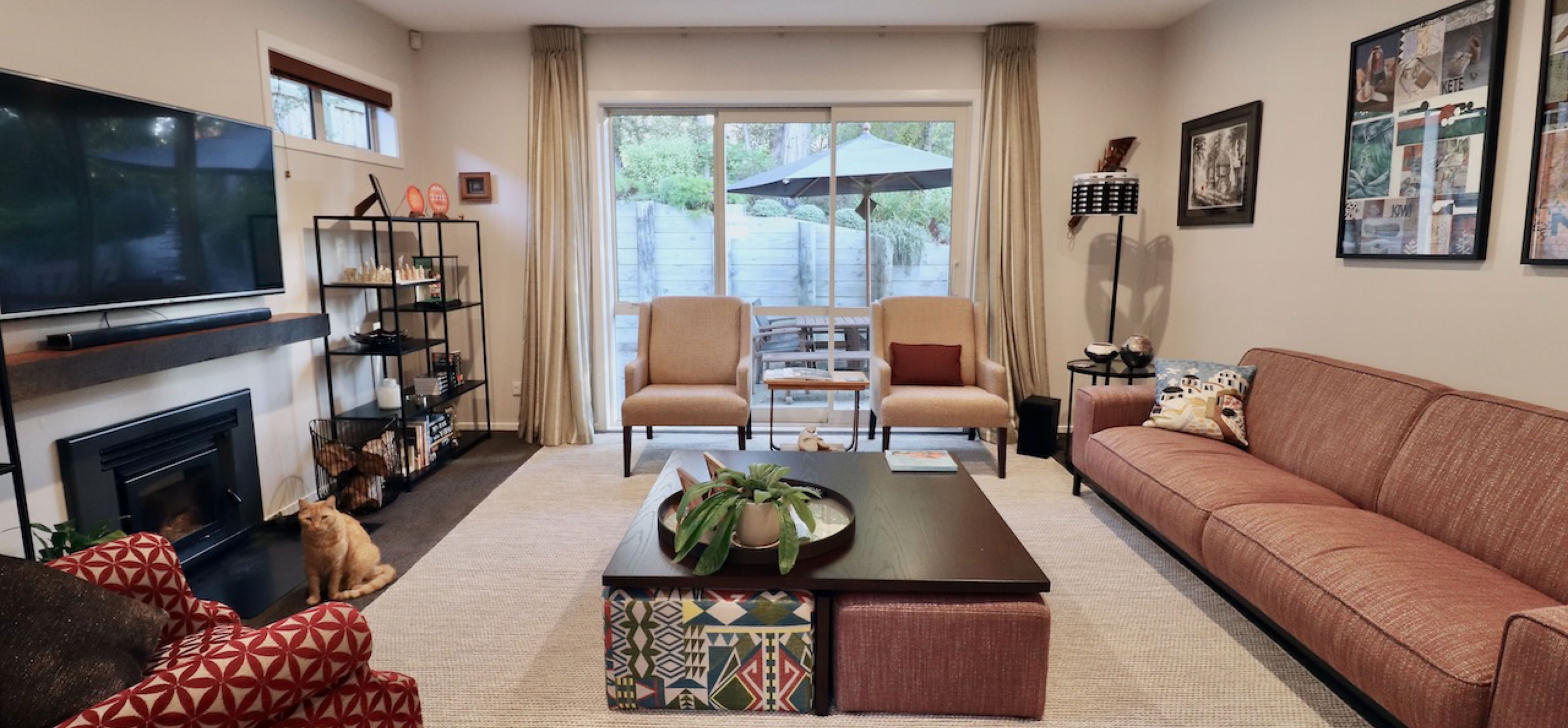 Studio 28 Interio Design Wellington Zealand. Creating wow interiors that are easy on the eye. Living room with light coloured rug over dark carpet. sofa and 3 chairs with coffee table and ottomans. TV wall is balalnced with shelving either side.